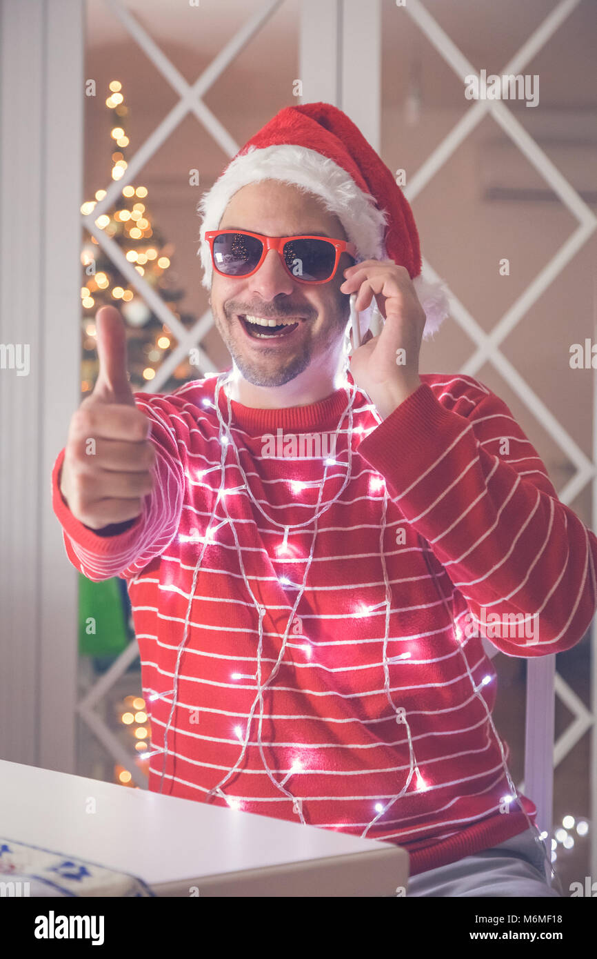 Portrait of young man wearing santa hat and sunglasses showing thumbs ...