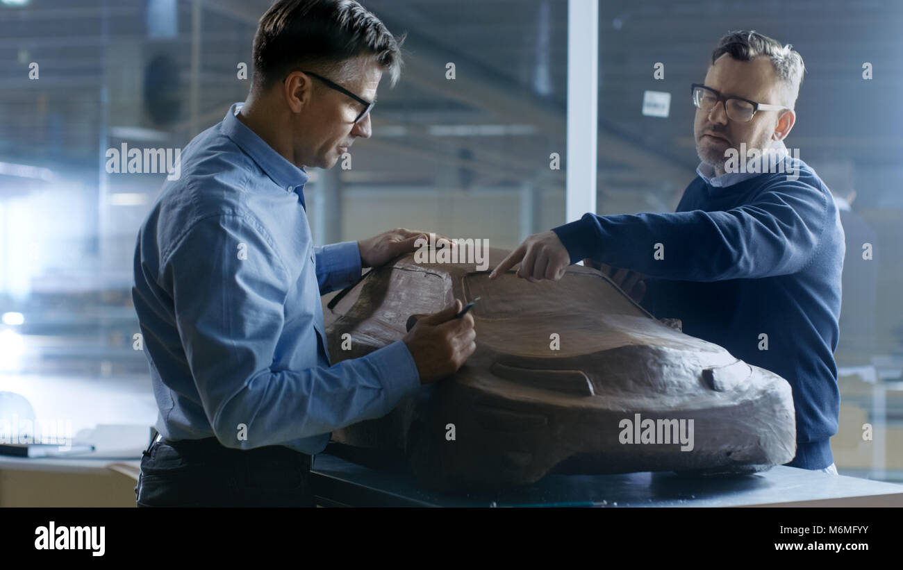 Two Male Automotive Designers Working on a Clay Model of New Generation Electric Car Future Design. One Holds Tablet Computer For Graphic Design, Othe Stock Photo