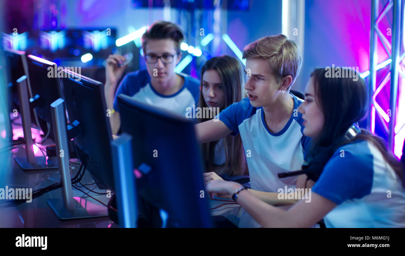 Team of Professional Boys and Girls Gamers Actively Thinking/ Discussing Game Strategy/ Tactic, They're In Internet Cafe or on Cyber Games Tournament. Stock Photo