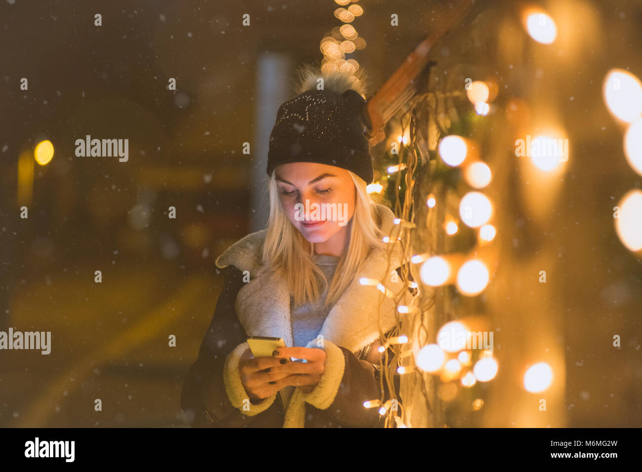 Portrait of beautiful woman using smartphone next to Christmas lights  decoration. Technology and holiday concepts Stock Photo - Alamy