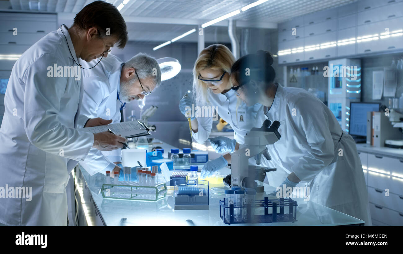 Team of Medical Research Scientists Work on a New Generation Disease Cure. They use Microscope, Test Tubes, Micropipette and Writing Down Results Stock Photo