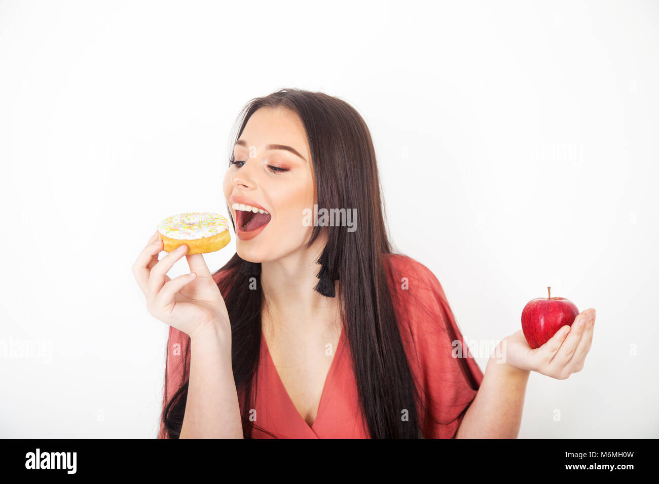 Pretty teenage girl taking a bite out of a donut and holding an apple in her hand. Stock Photo