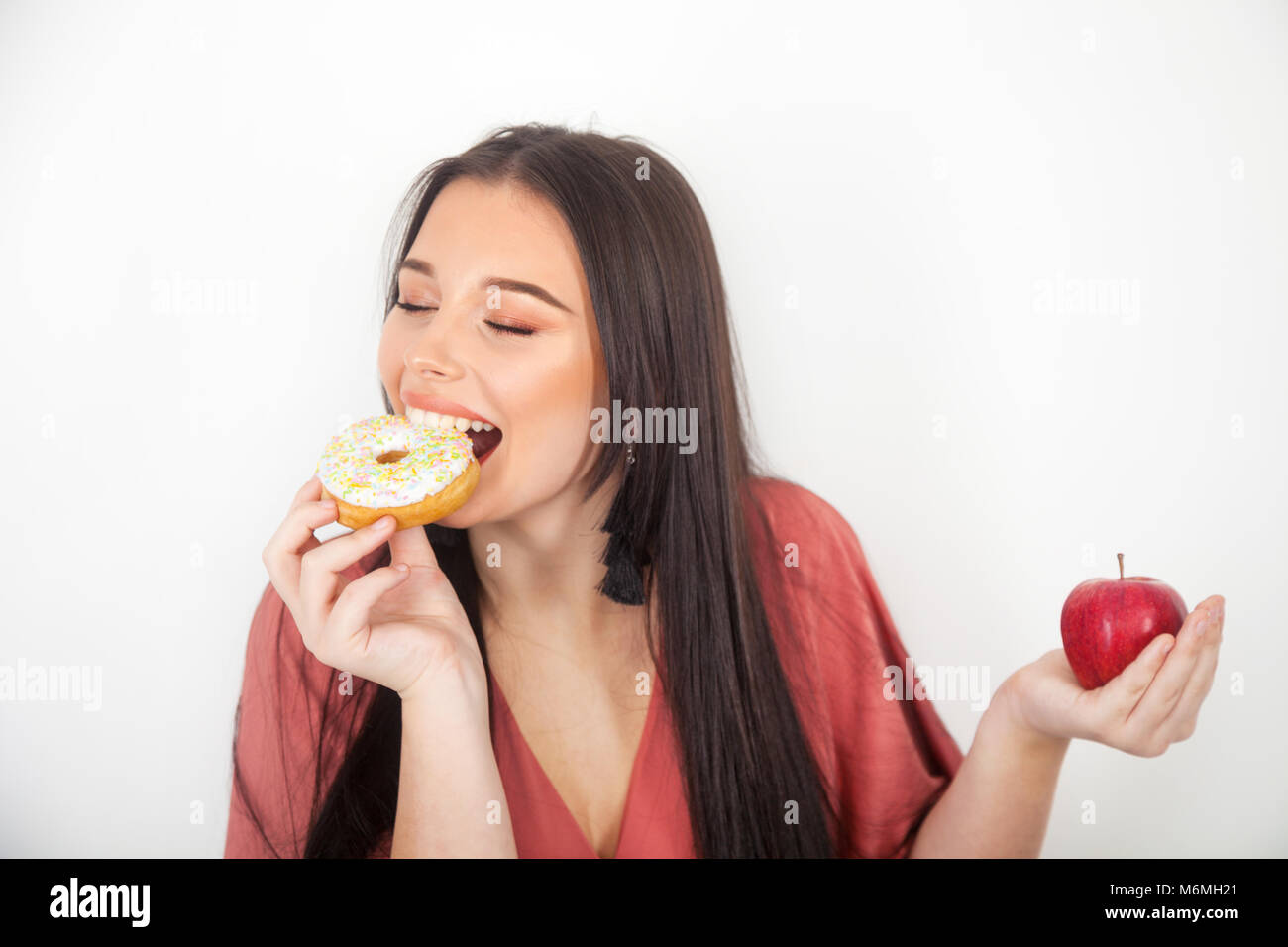 Pretty teenage girl taking a bite out of a donut and holding an apple in her hand. Stock Photo