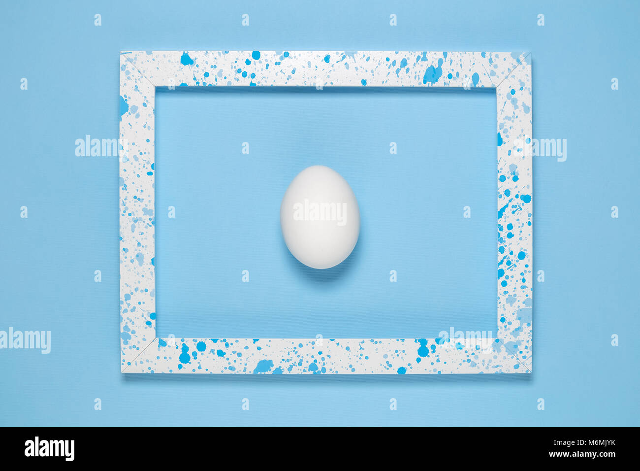 Flat lay of white egg in wooden frame colored with blue paint splatters