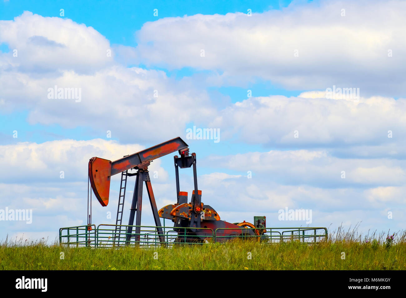 Colorful pump jack on oil well - low horizon on prairie with green grass and wild flowers - big blue cloudy sky - room for text Stock Photo