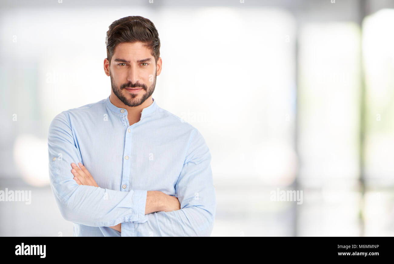 Portrait of a young man standing with arms crossed while looking at ...