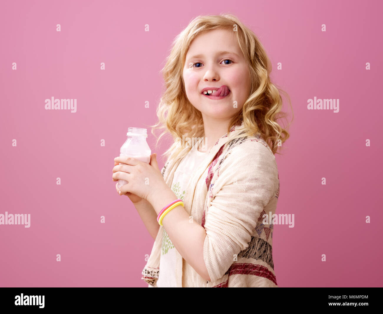 Pink mood. smiling stylish girl with wavy blonde hair isolated on pink background with delicious farm organic yogurt licking lips Stock Photo