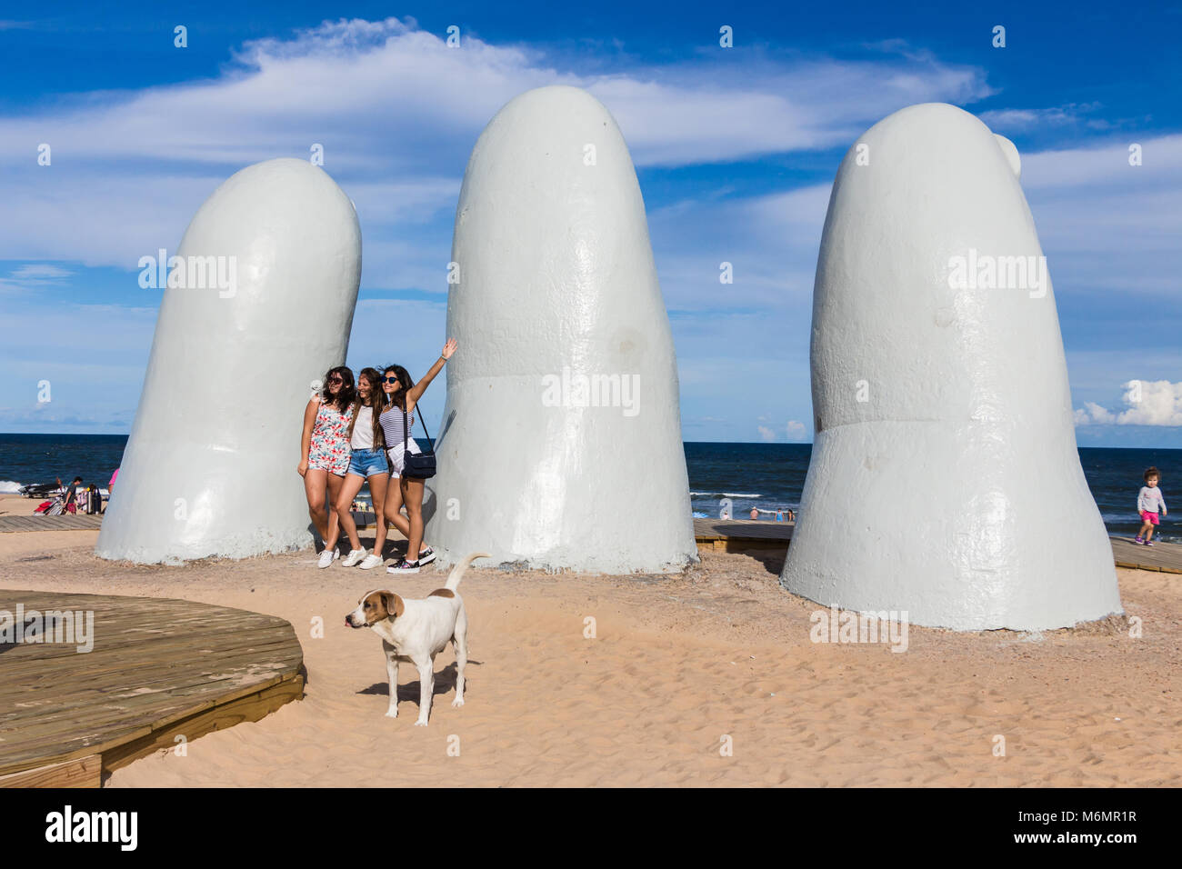 Punta Del Este, Uruguay - February 28th, 2018: Three young women taking photos and sefies at La Mano, the sculpture made by Mario Irarrazabal, Playa L Stock Photo