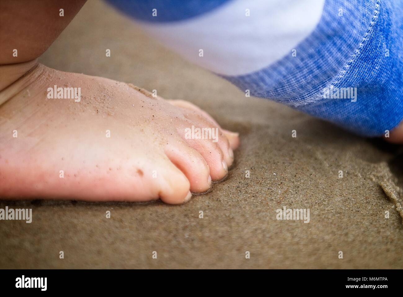 Happy bare feet on sandy beach. Feet covered in sand. Sunny. Shallow depth of field. Stock Photo