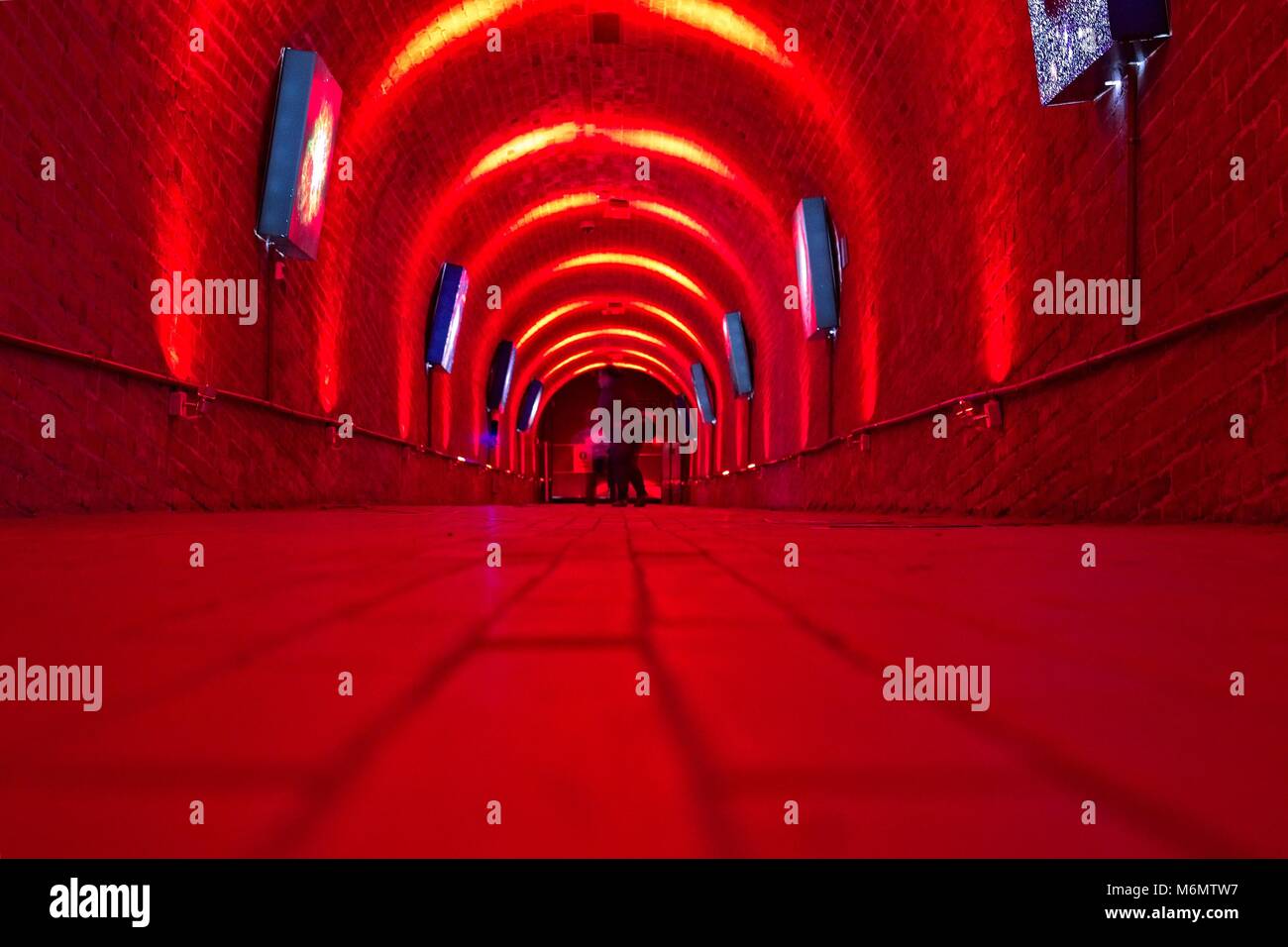 Red corridor with blueish artwork. View from the floor level. Two people at the far end. Stock Photo