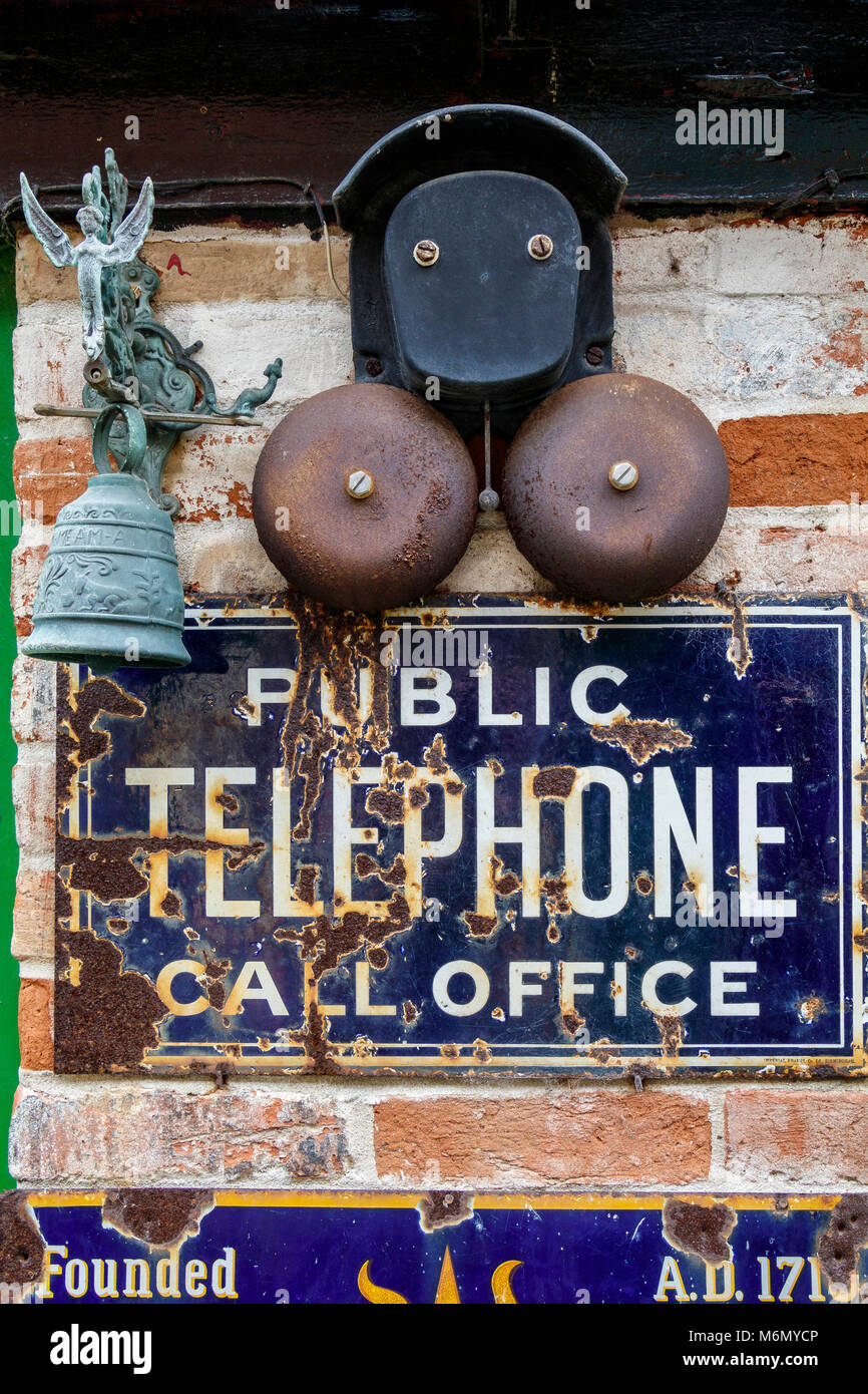Sign for the Public Telephone Call Office with bell mounted above and unrelated metal bell with angel on top. North Walsham, Norfolk, UK. Stock Photo