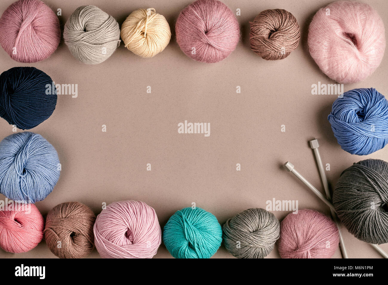 A group of colored balls of yarn and knitting needles on a beige