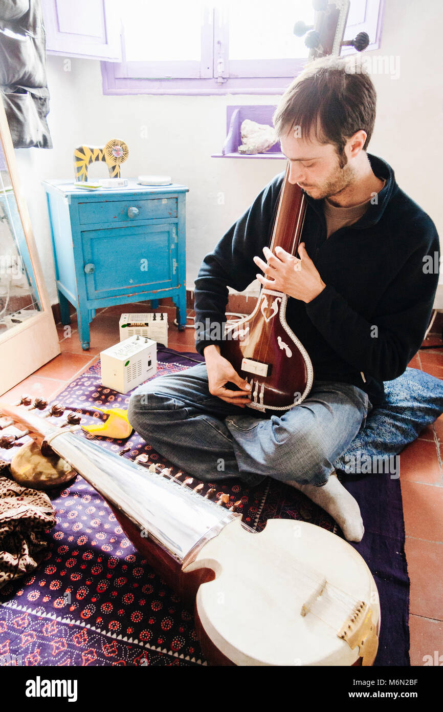 Young man playing Indian classical music on a sarod at home in the Albaicin district of Granada, Andalusia, Spain. Stock Photo