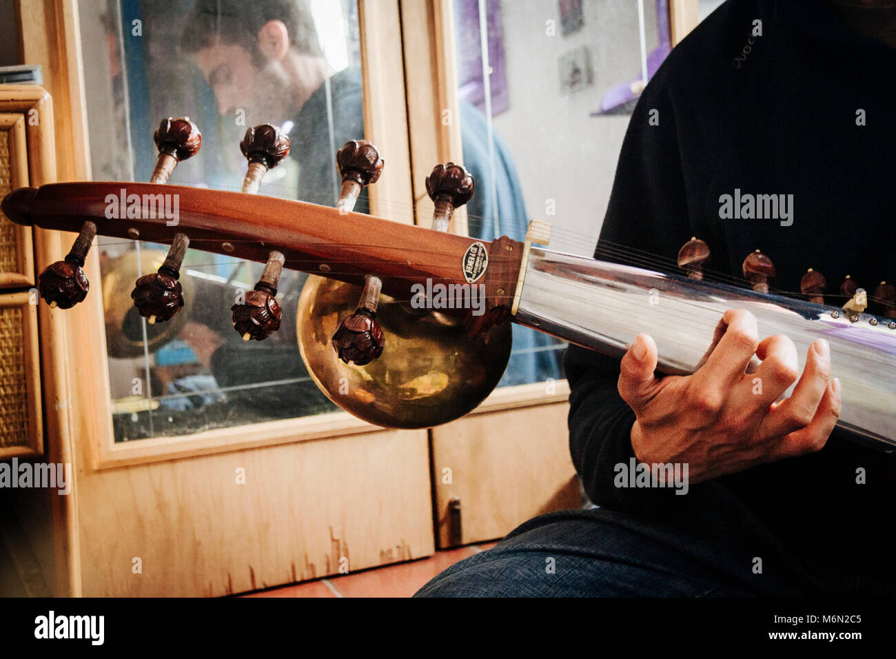 Young man playing Indian classical music on a sarod at home in the Albaicin district of Granada, Andalusia, Spain. Stock Photo