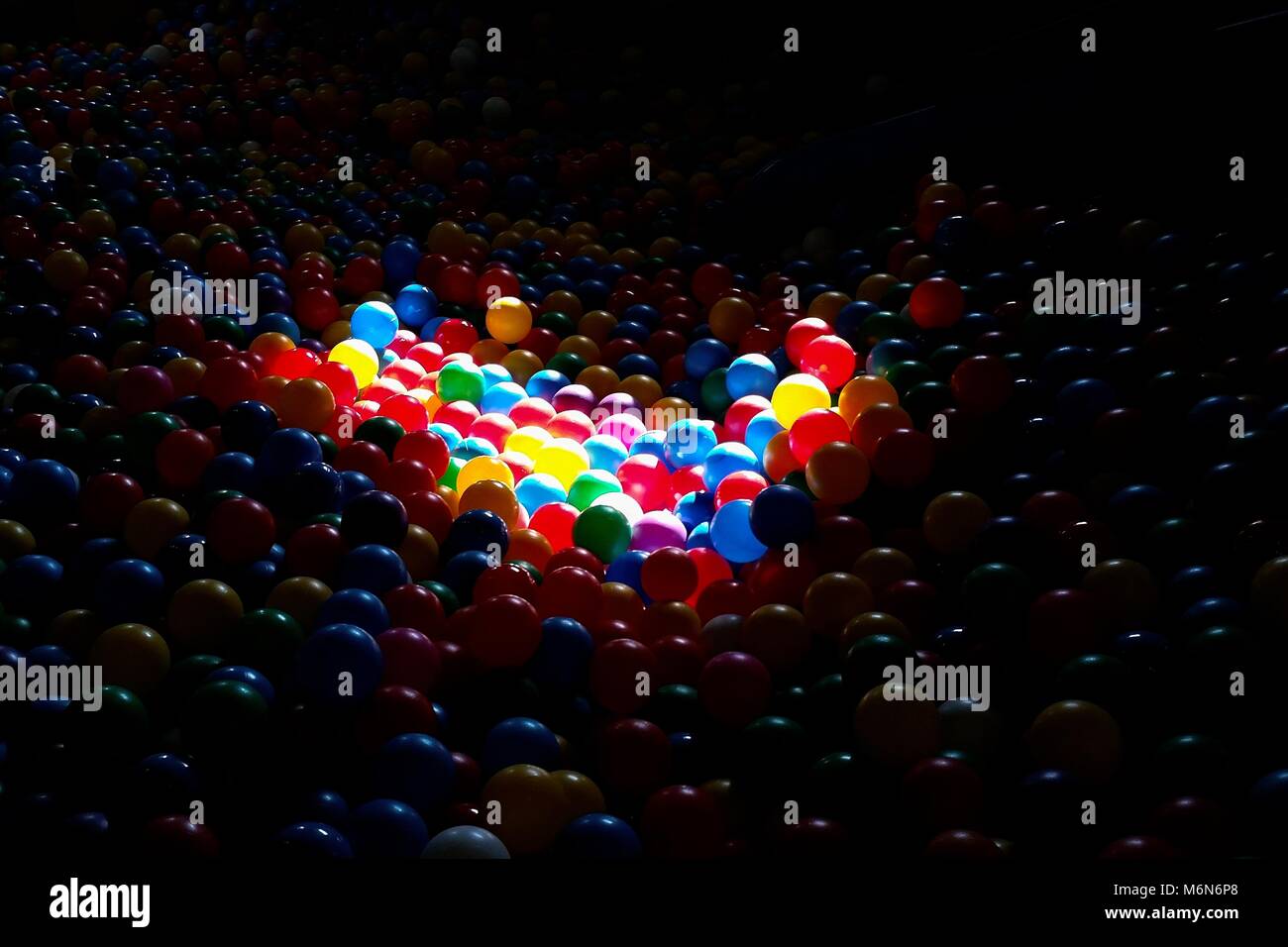 Colorful plastic balls in the playground. Lightened by sun, creating big contrast with dark surrounding. Stock Photo