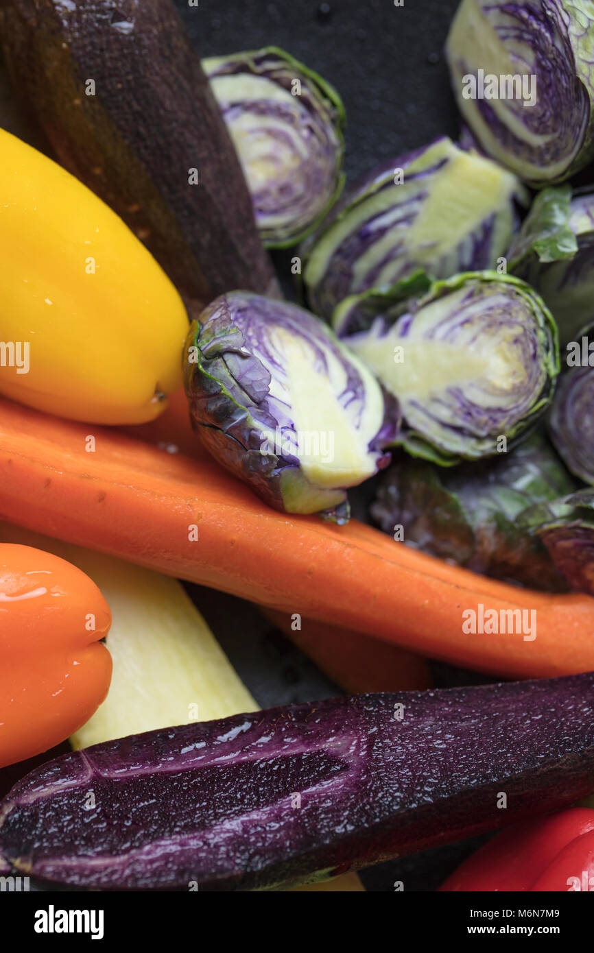 Mixed purple Brussels Spouts, colorful carrots and yellow, red and orange bell peppers being prepped for pan roasting in the oven Stock Photo