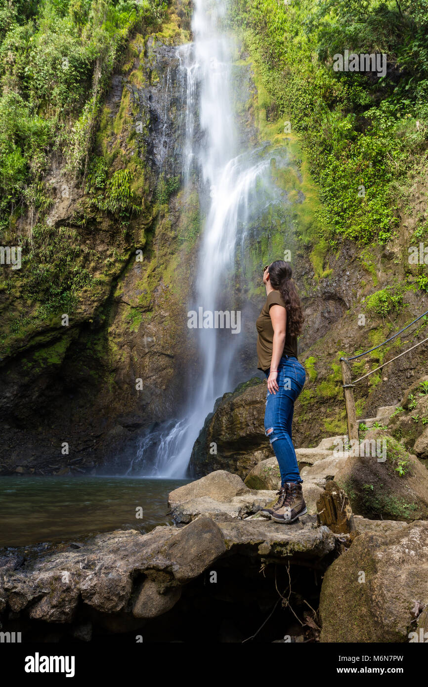 young woman standing in front of a beautiful waterfall in tropical ...