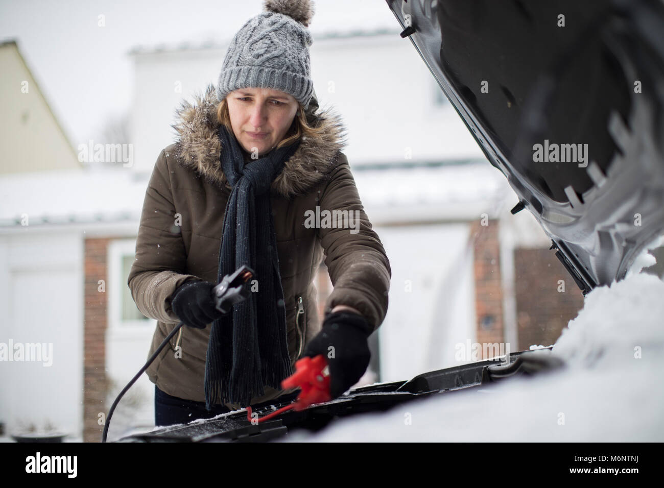 Woman Using Jumper Cables On Car Battery On Snowy Day Stock Photo