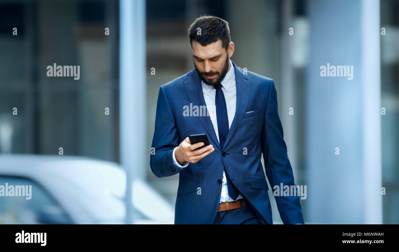 Successful Business Man Uses Smartphone While Walking on the Big City Business District Street. Stock Photo