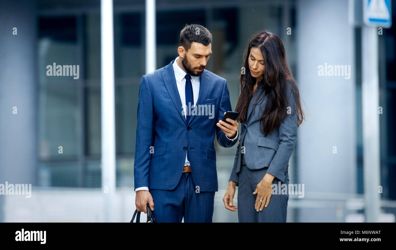 Business Woman and Business Man Use Smartphone and Talk on the Busy Big City Street. Both Look Exquisitely Stylish. Stock Photo