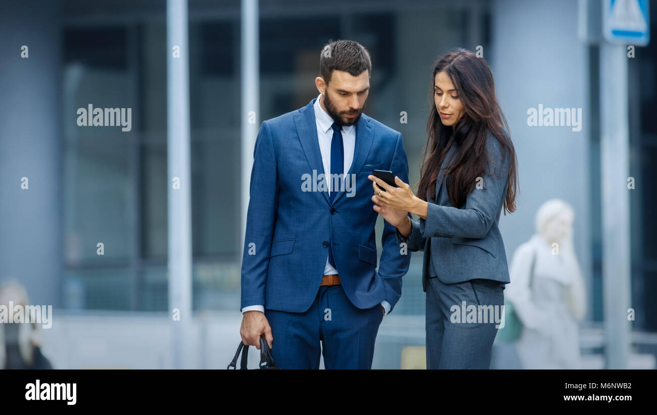 Business Woman and Business Man Use Smartphone and Talk on the Busy Big City Street. Both Look Exquisitely Stylish. Stock Photo