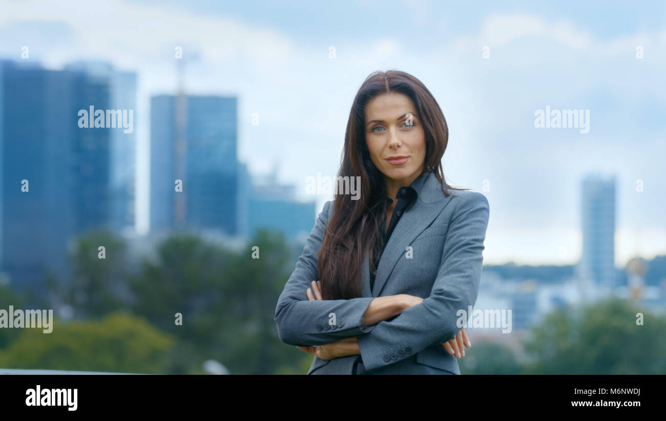 Successful Business Woman Crosses Arms and Smiles in the Background Skyscrapers and Business Centre of the Big City is Visible. Stock Photo