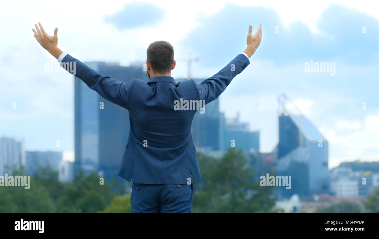 Happy Successful Business Man Raises His Hands, He Has His Business Victory. In The Background Big City with Skyscrapers. Stock Photo