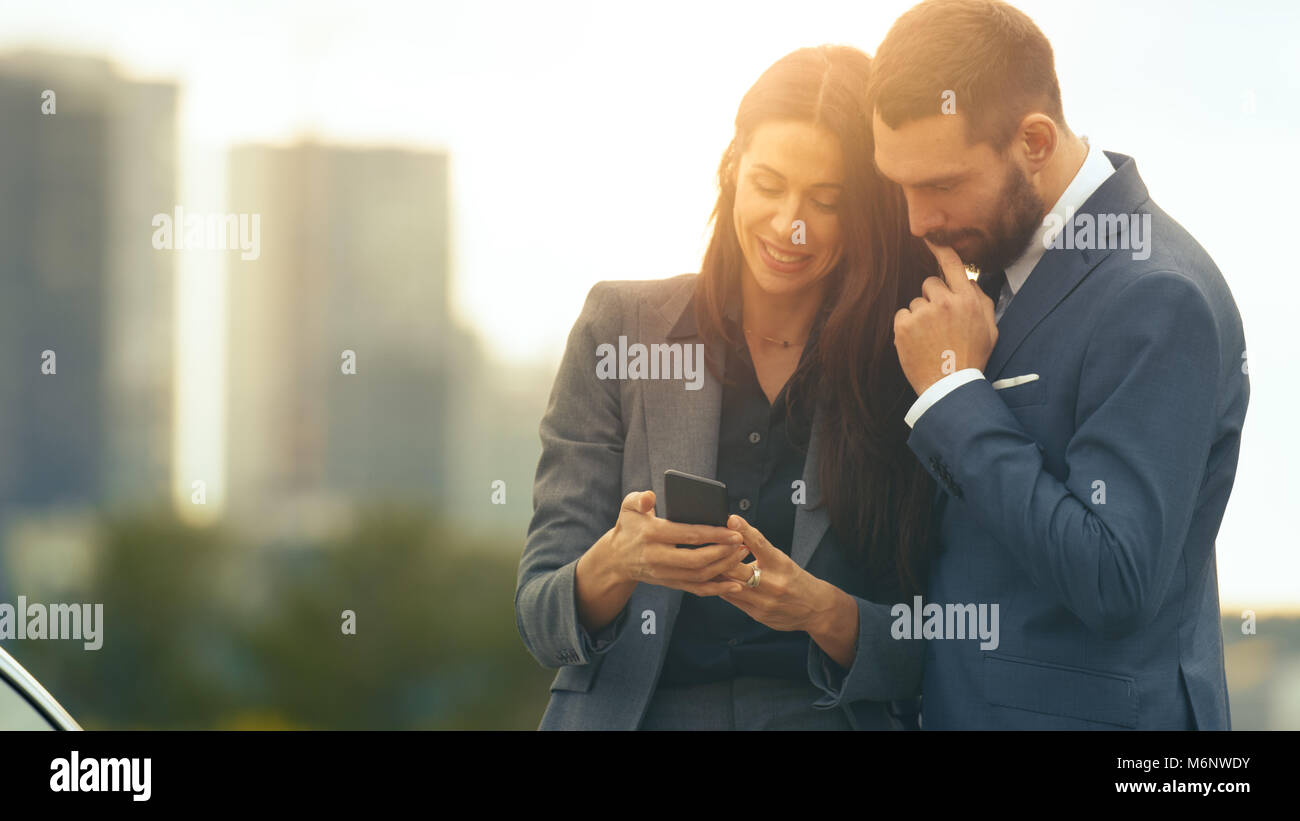 Beauty Young Couple of Business Man and Business Woman Use Smartphone and Share it. Big City with Skyscrapers in the Background. Stock Photo