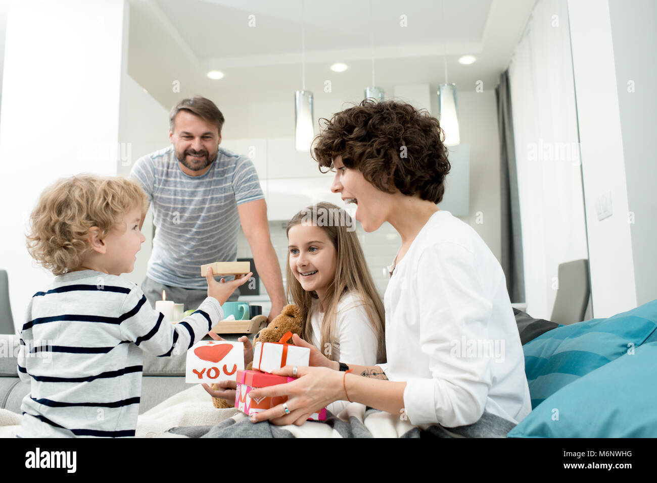 Portrait of happy young family with two children celebrating Valentines day  at home with adorable little boy giving presents in foreground Stock Photo