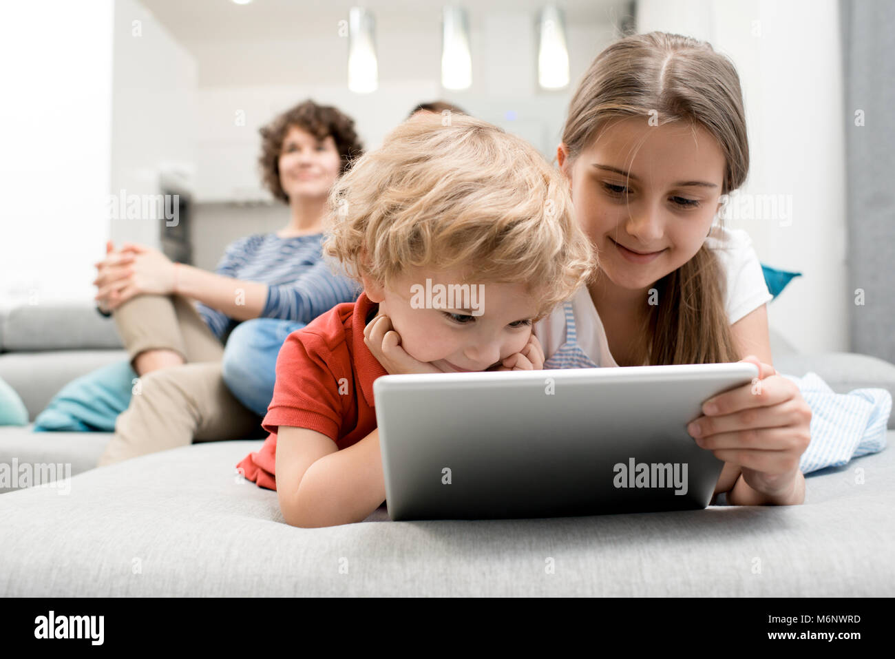 Portrait of brother and sister using digital tablet lying on sofa in ...