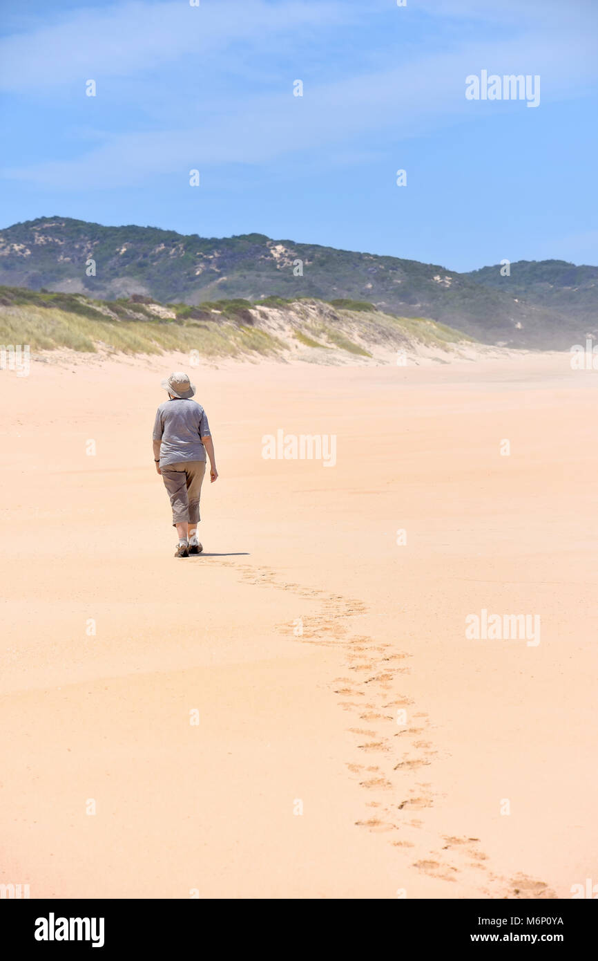 A female on a clean beach at Goukamma near Knysna on the garden route in South Africa walking in isolation determined straight ahead into the distance Stock Photo