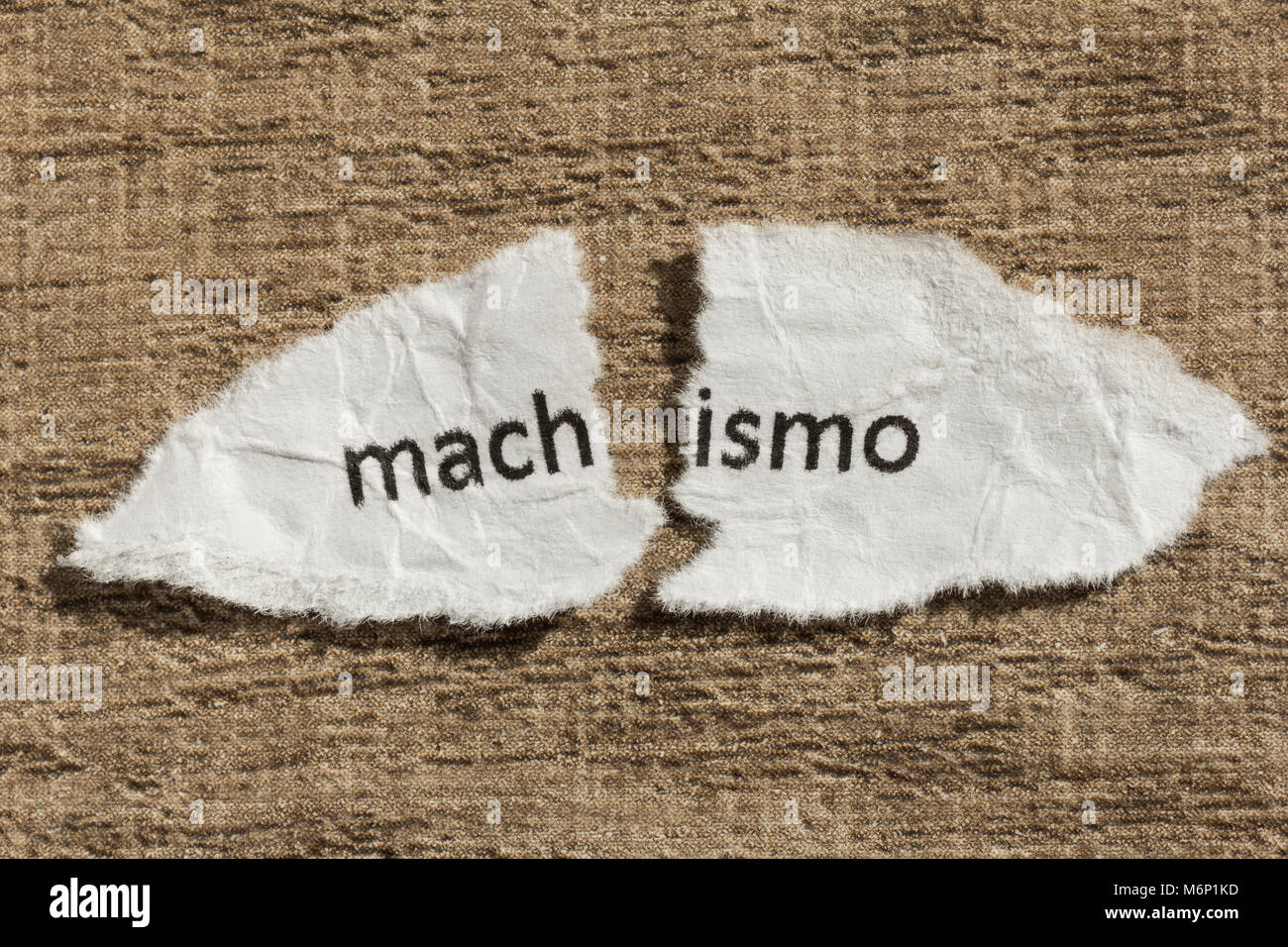 Torn paper written machismo, portuguese and spanish word for chauvism, over wooden background. Old and abandoned idea or practice. Macro photography. Stock Photo