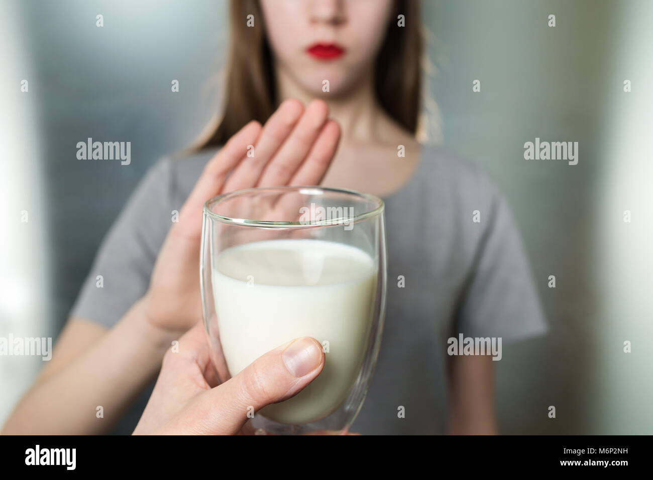 Lactose intolerance. Dairy Intolerant young girl refuses to drink milk - shallow depth of field. Selective focus on glass of milk Stock Photo