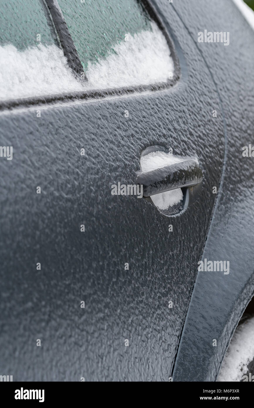 Dark grey car door covered in black ice on a sub zero winter morning caused by freezing rain. Potential copy space to the left of door handle. Stock Photo
