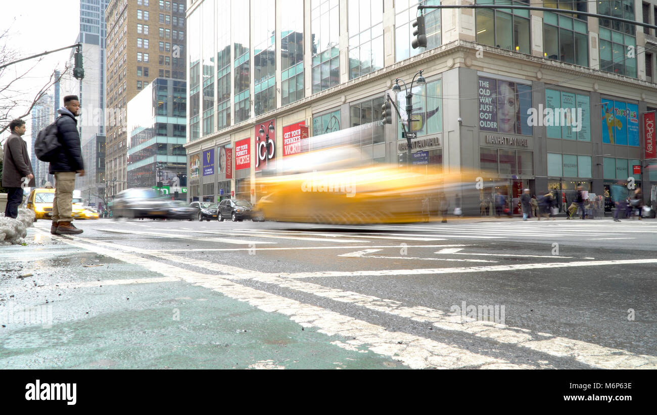 New York City - Circa 2017: Motion blur effect of yellow NYC taxi cab crossing crosswalk intersection in midtown Manhattan. People wait to safely cros Stock Photo