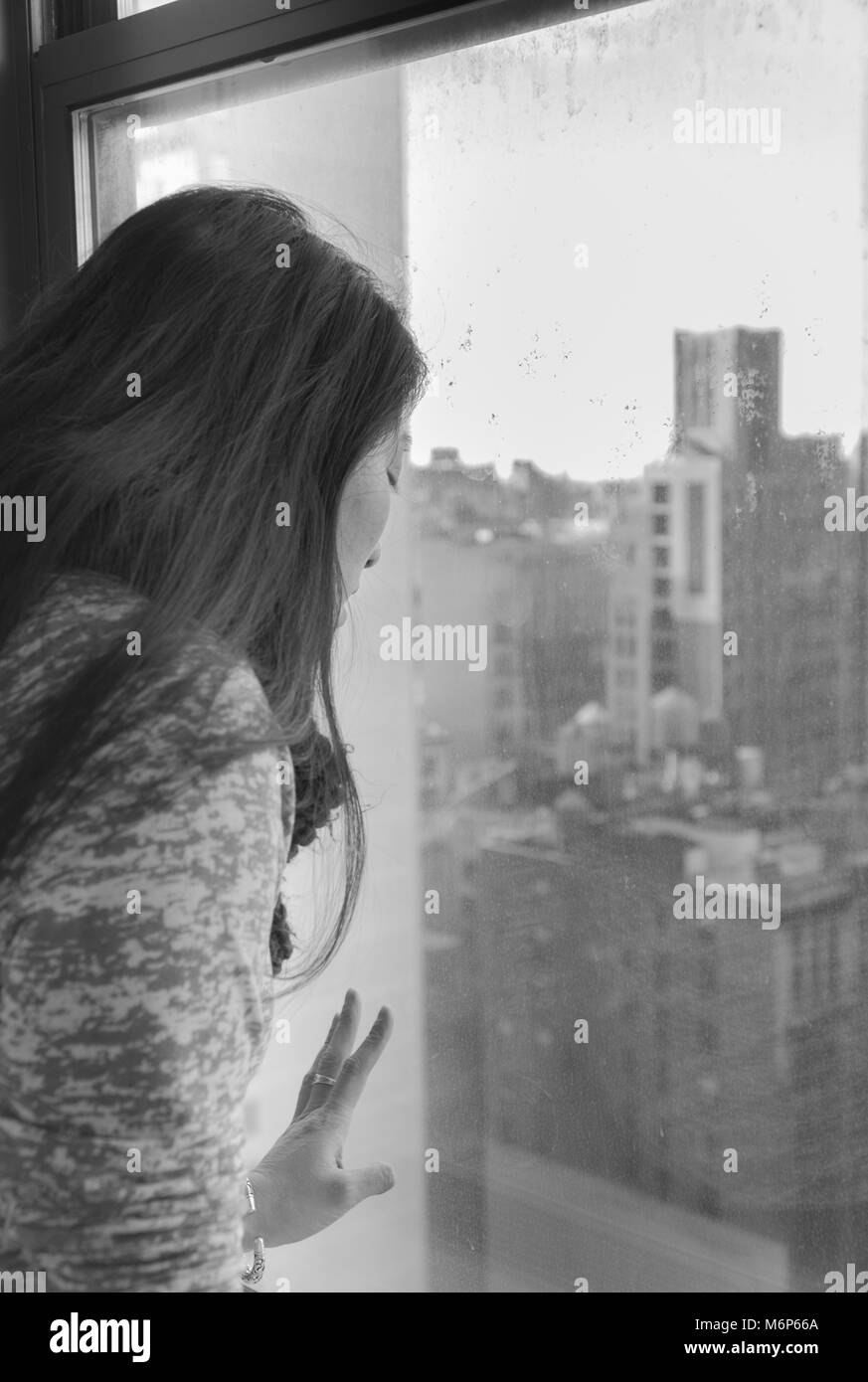 Young asian woman looking through a window birds eye view overlooking New York City skyline on a sunny day. Tourist traveling seeing attractions - bla Stock Photo