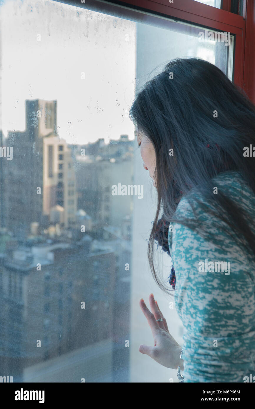 Young asian woman staring through a window birds eye view overlooking New York City skyline on a sunny day. Tourist traveling seeing attractions  - Ve Stock Photo