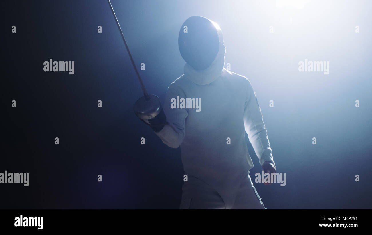 Fully Equipped Fencer Puts Lifts Foil Sword in Readiness for a Match. He Stands in the Spotlight while Darkness is Around Him. Shot Isolated on Black Stock Photo
