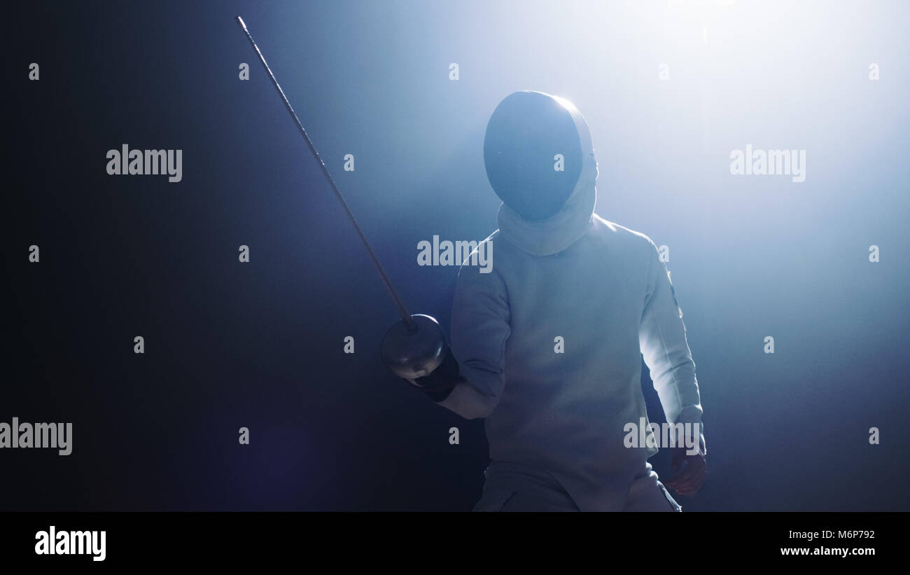 Fully Equipped Fencer Puts Lifts Foil Sword in Readiness for a Match. He Stands in the Spotlight while Darkness is Around Him. Shot Isolated on Black  Stock Photo