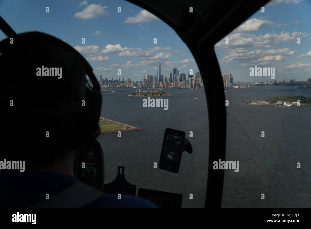 Aerial view over the shoulder of helicopter pilot looking at downtown New York City skyline during the day flying over harbor Stock Photo