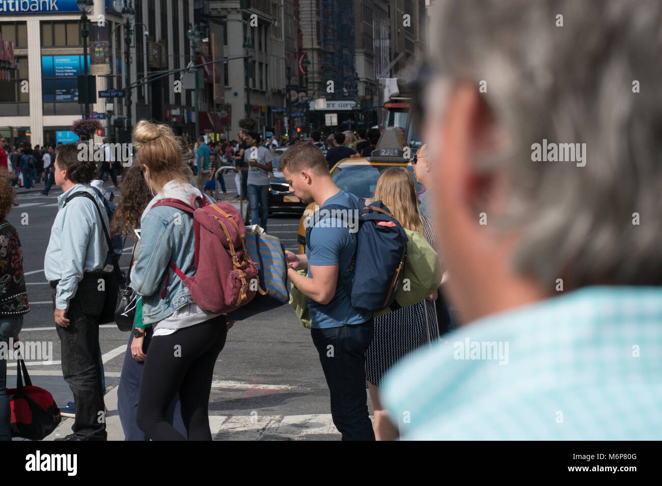 New York City, Circa 2017: Busy manhattan crosswalk intersection over the shoulder of man waiting to safely cross street during day time Stock Photo
