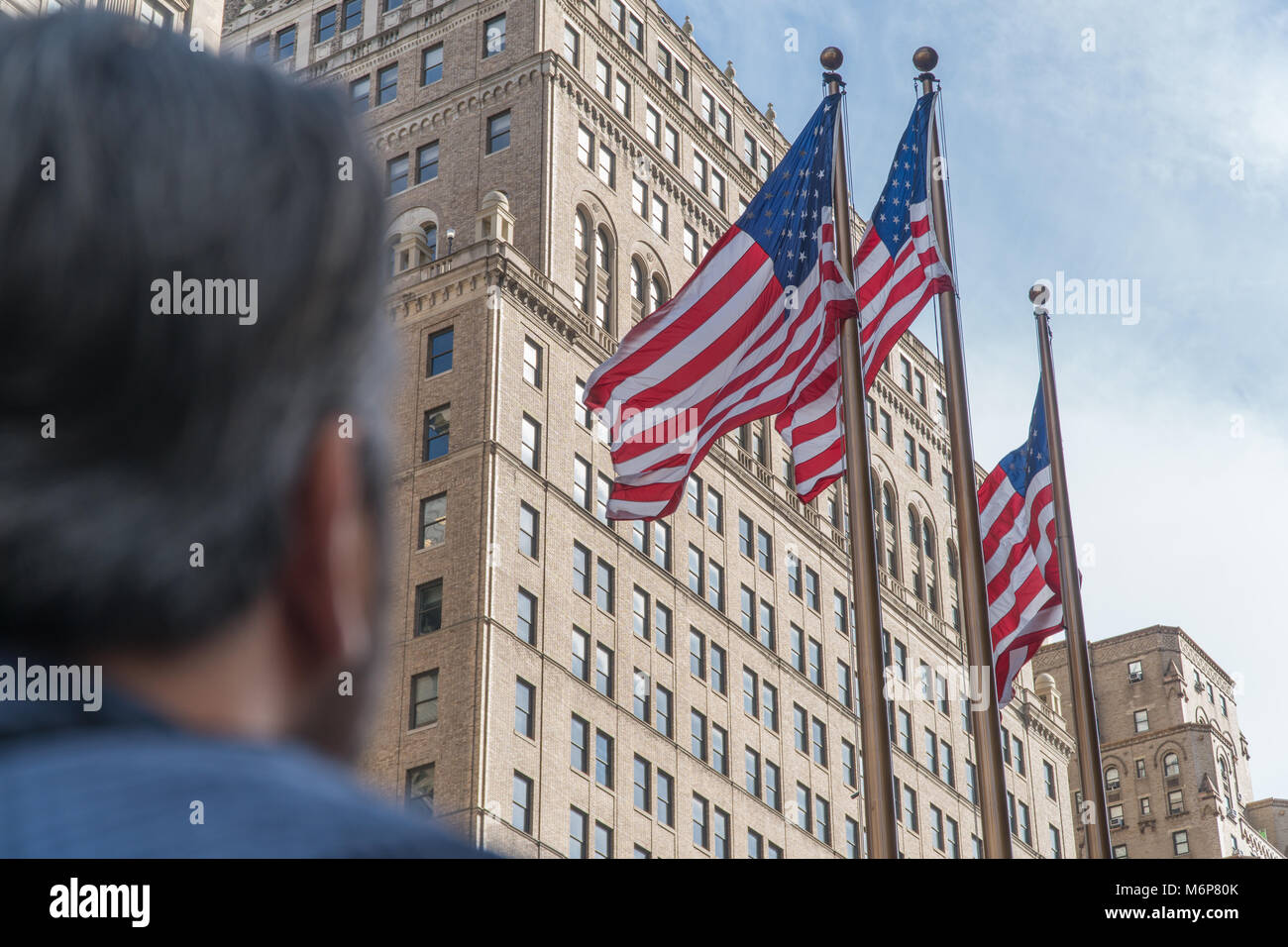 Young man looks up to American flags flying tall on wind day. Salute to independence and freedom USA Stock Photo