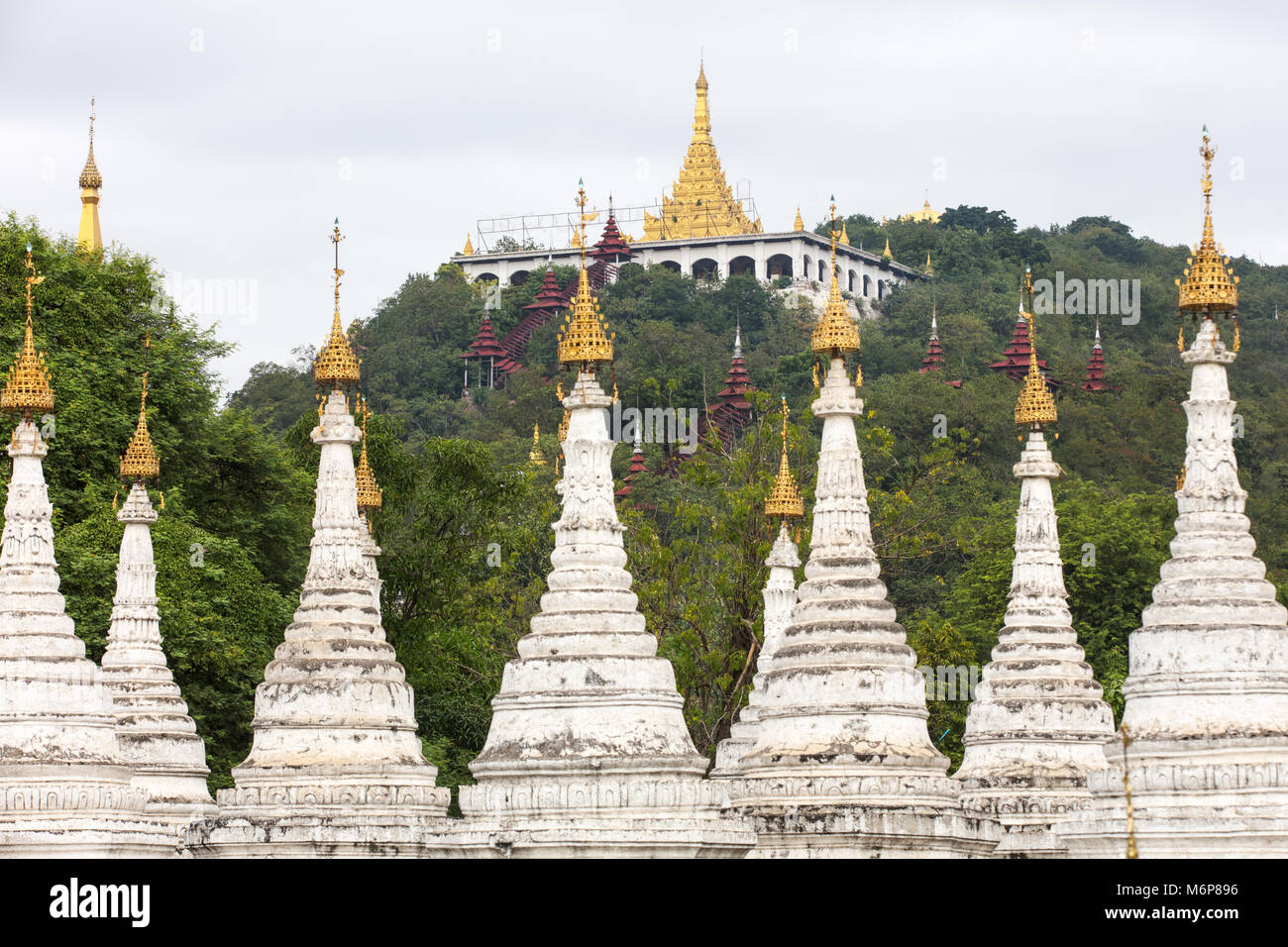 The white stupas of the Sandamuni Pagoda with the Mandalay Hill in the background.. Myanmar (Burma). Stock Photo
