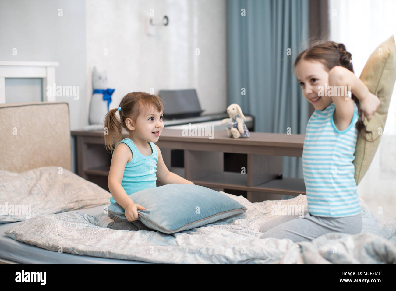Little kids sisters fighting using pillows in bedroom Stock Photo