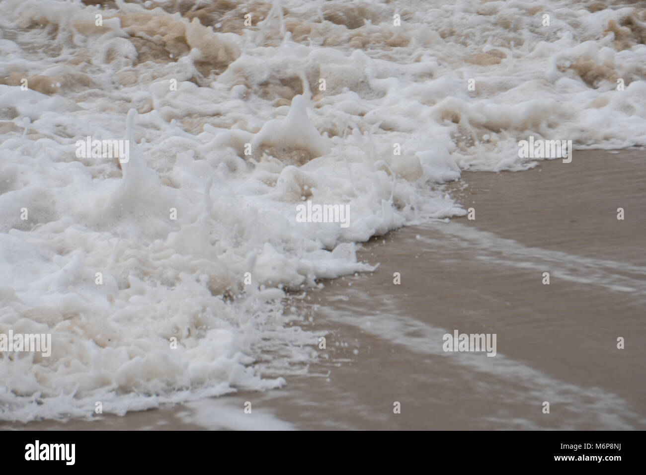 Ocean waves crash on a sandy beach in day time. Rip current pull water back from shore out to sea Stock Photo