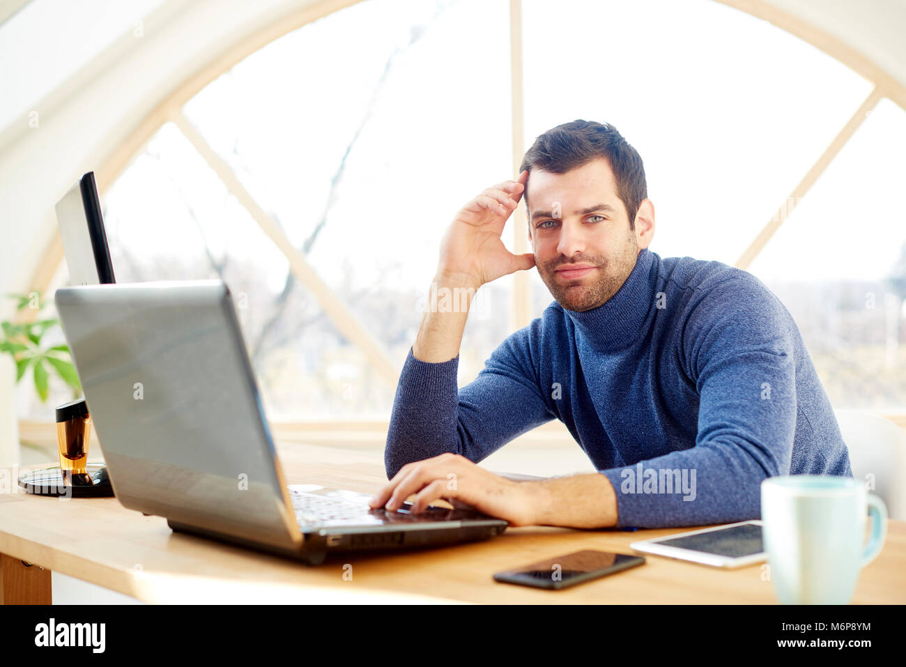 Portrait of young man with his forehead rested on his hand and looking ...