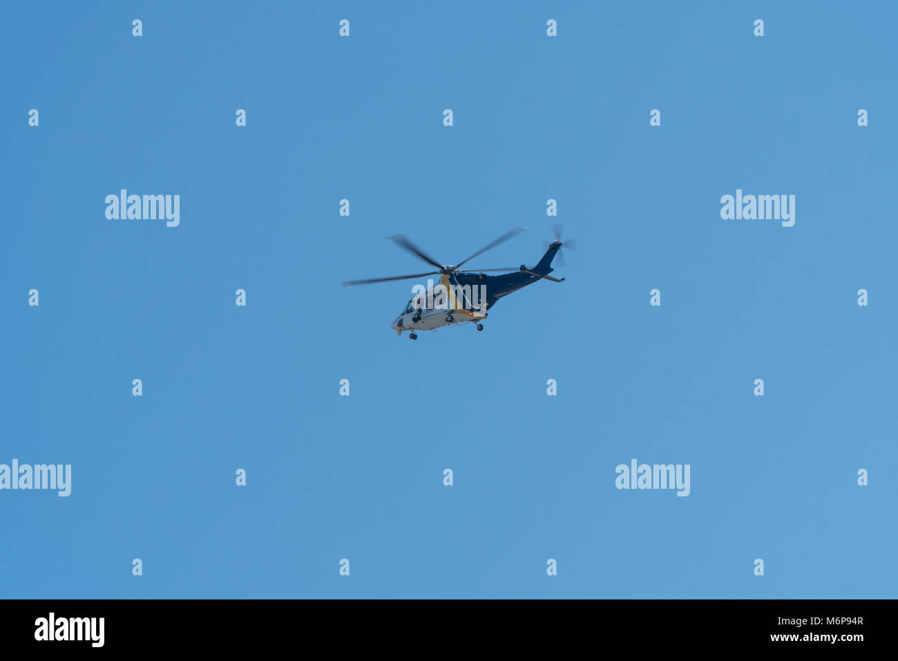 Generic blue and white police helicopter with visual camera surveillance equipment fly in sky high above city aerial patrol Stock Photo