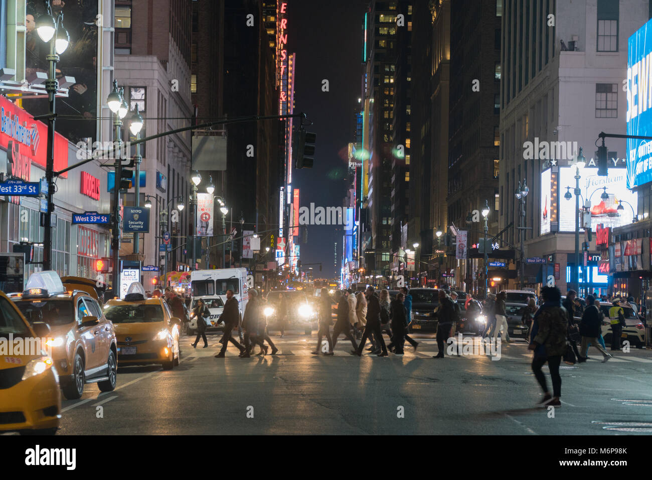 New York City, Circa 2017: Night time wide angle view of midtown Manhattan NYC crosswalk during rush hour. People walk safely across avenue intersecti Stock Photo