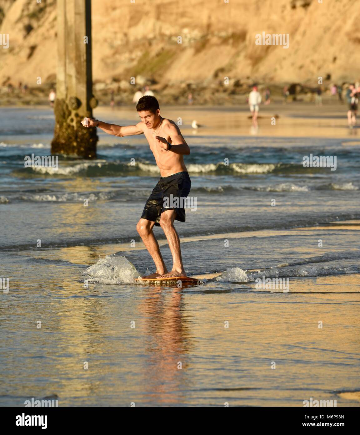 Young man on a skim board, skimming, at beach during sunset, gliding