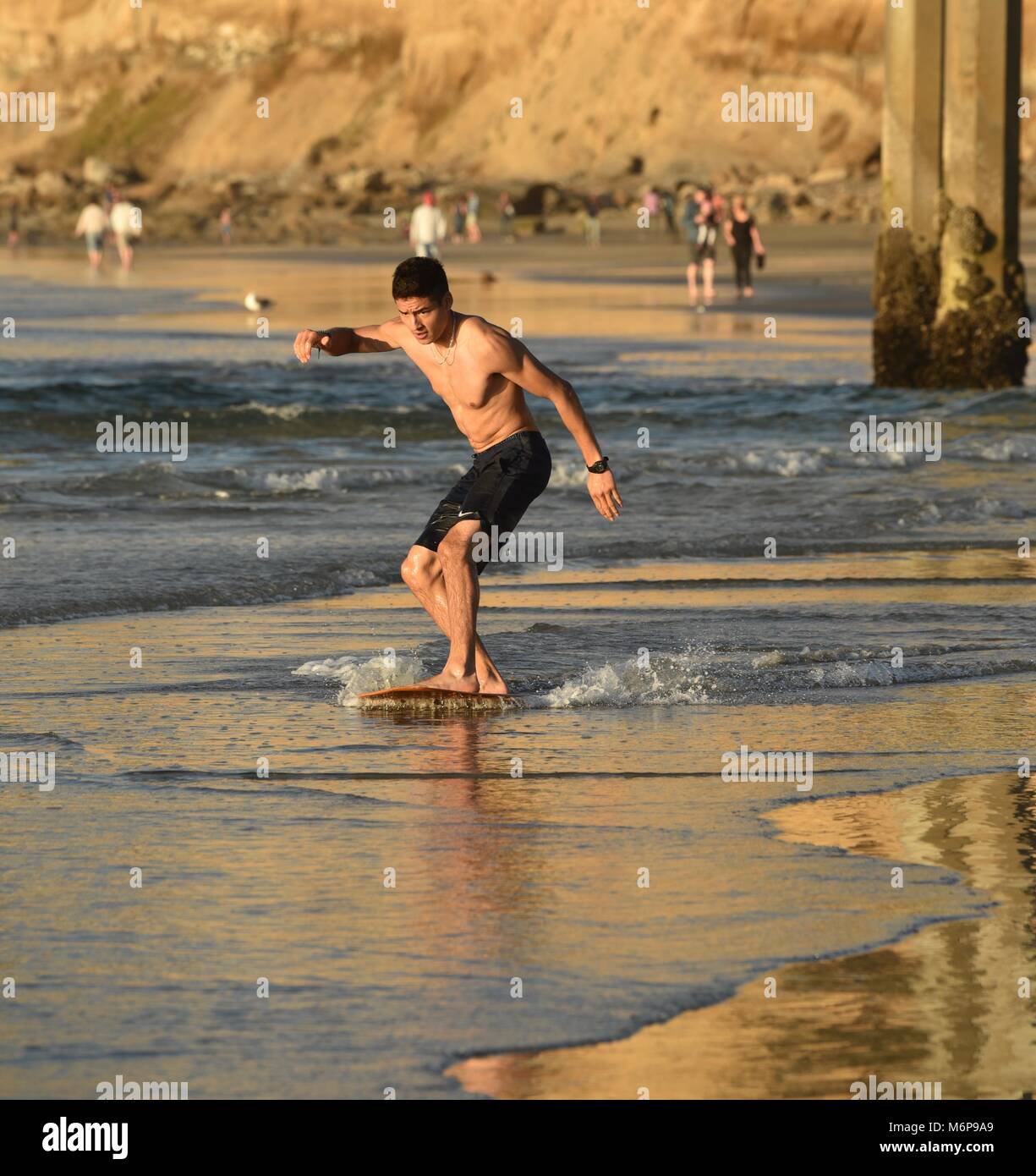 Young man on a skim board, skimming, at beach during sunset, gliding
